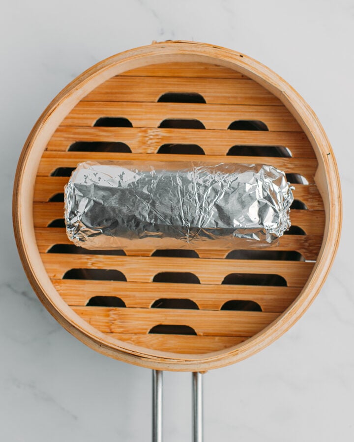 Log of seitan wrapped with aluminum foil on a bamboo steamer basket.