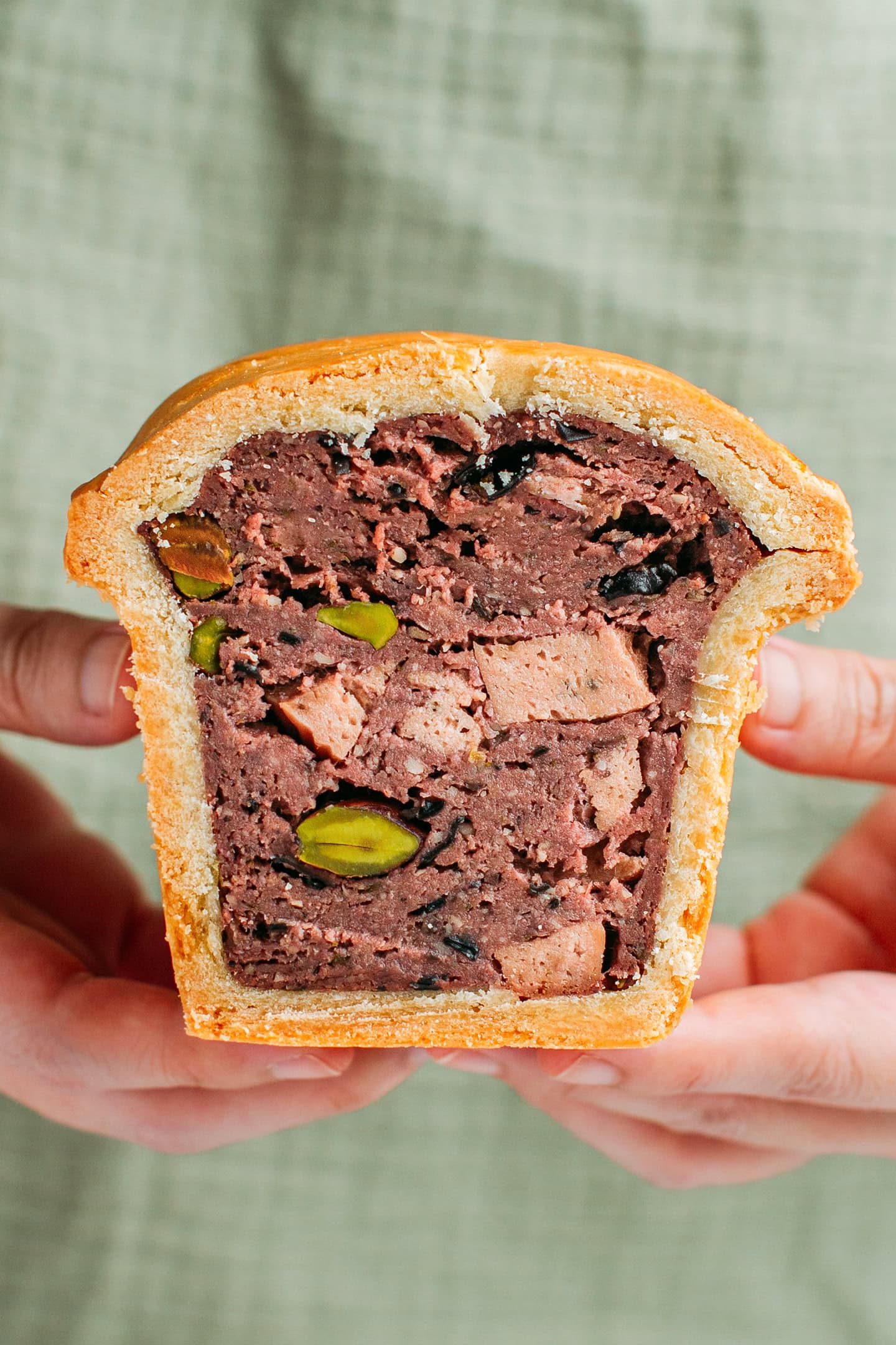 Holding a slice of vegan terrine pie filled with bologna and pistachios.