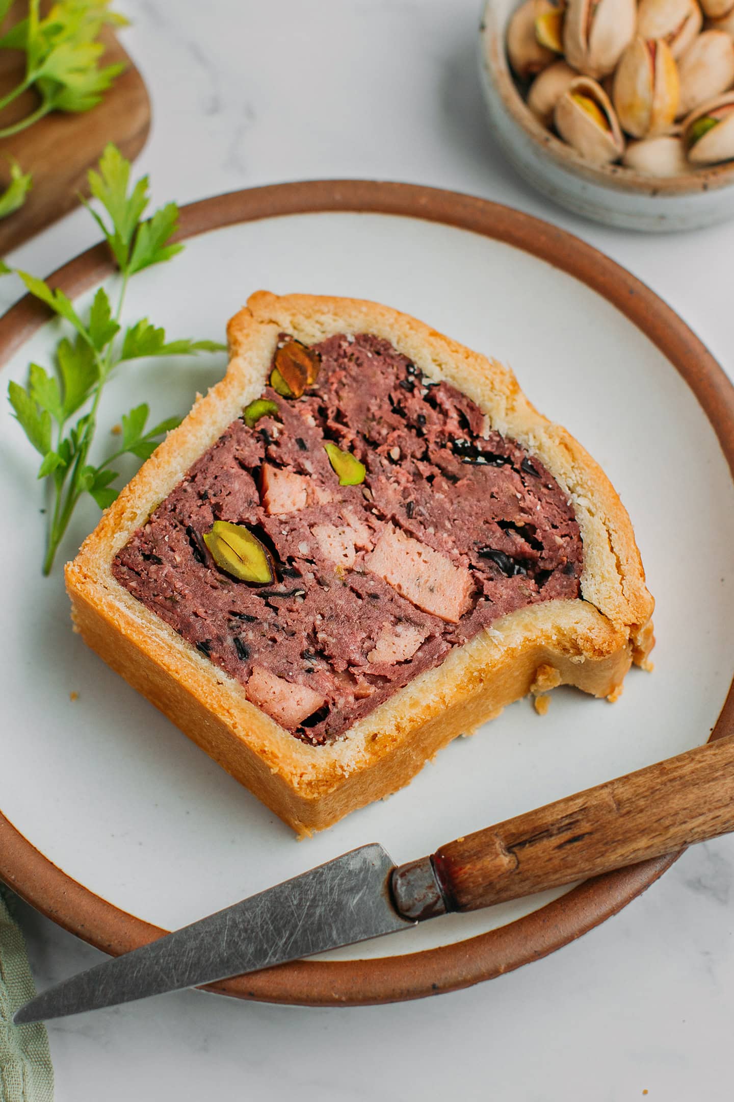 Slice of vegan pâté en croute filled with pistachios, bologna, and mushrooms.