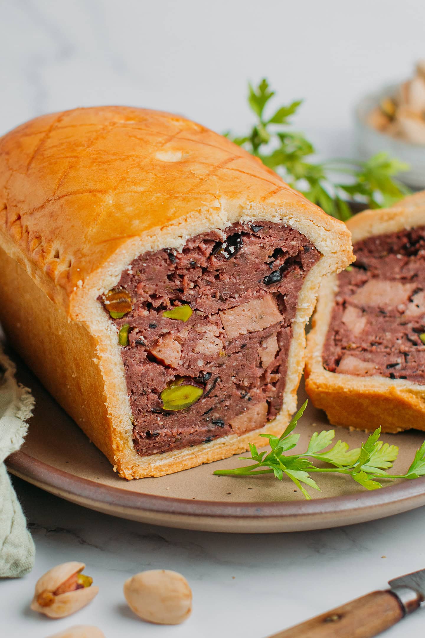 Close-up of a vegan terrine pie with mushroom filling and golden brown crust on a brown plate.