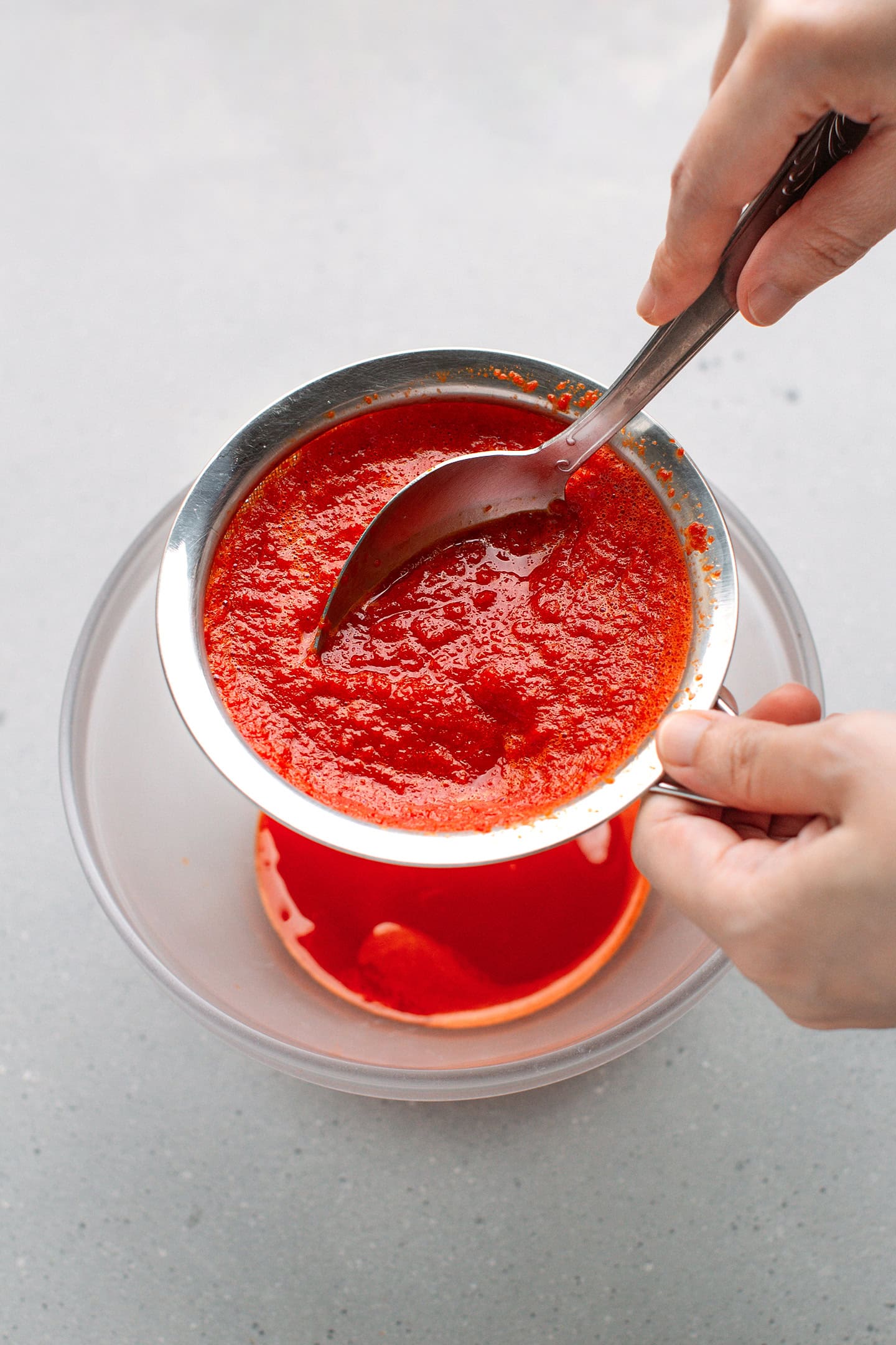 Straining puréed cayenne peppers through a fine-sieve mesh.