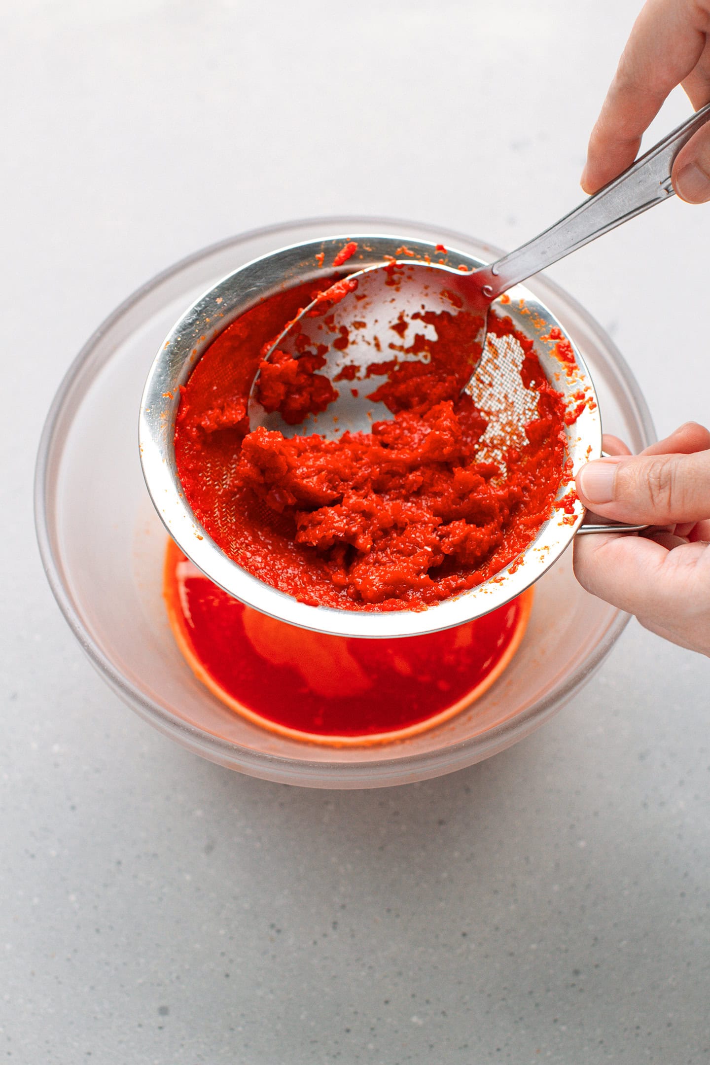 Straining chili sauce through a fine-mesh sieve.