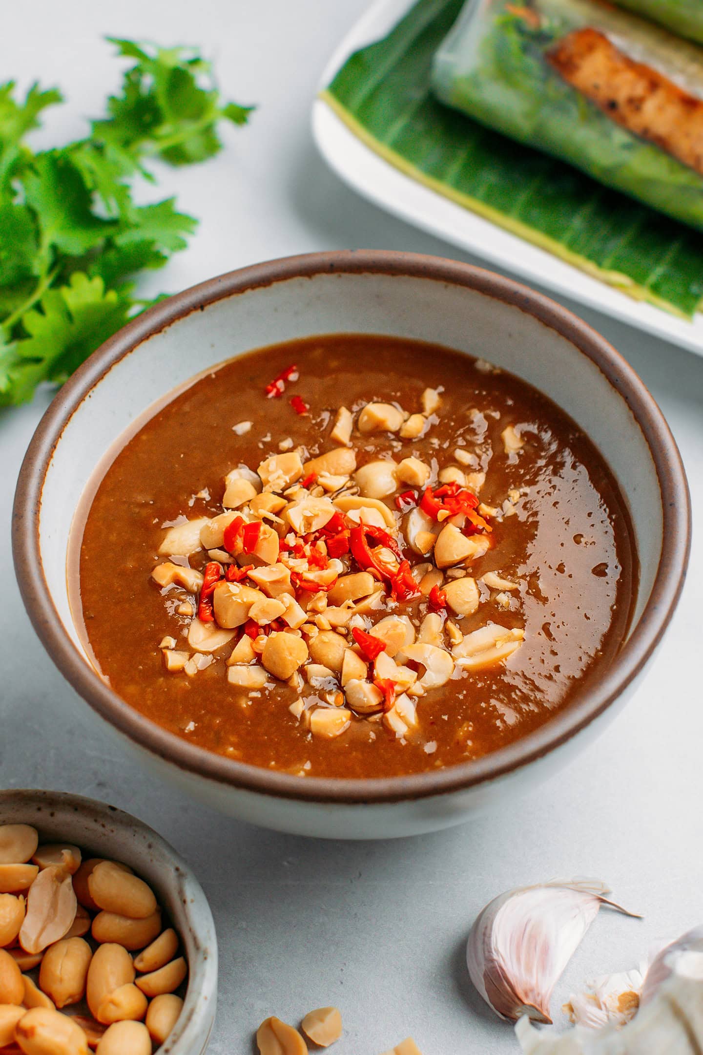 Peanut dipping sauce topped with crushed peanuts and chopped chili in a bowl.