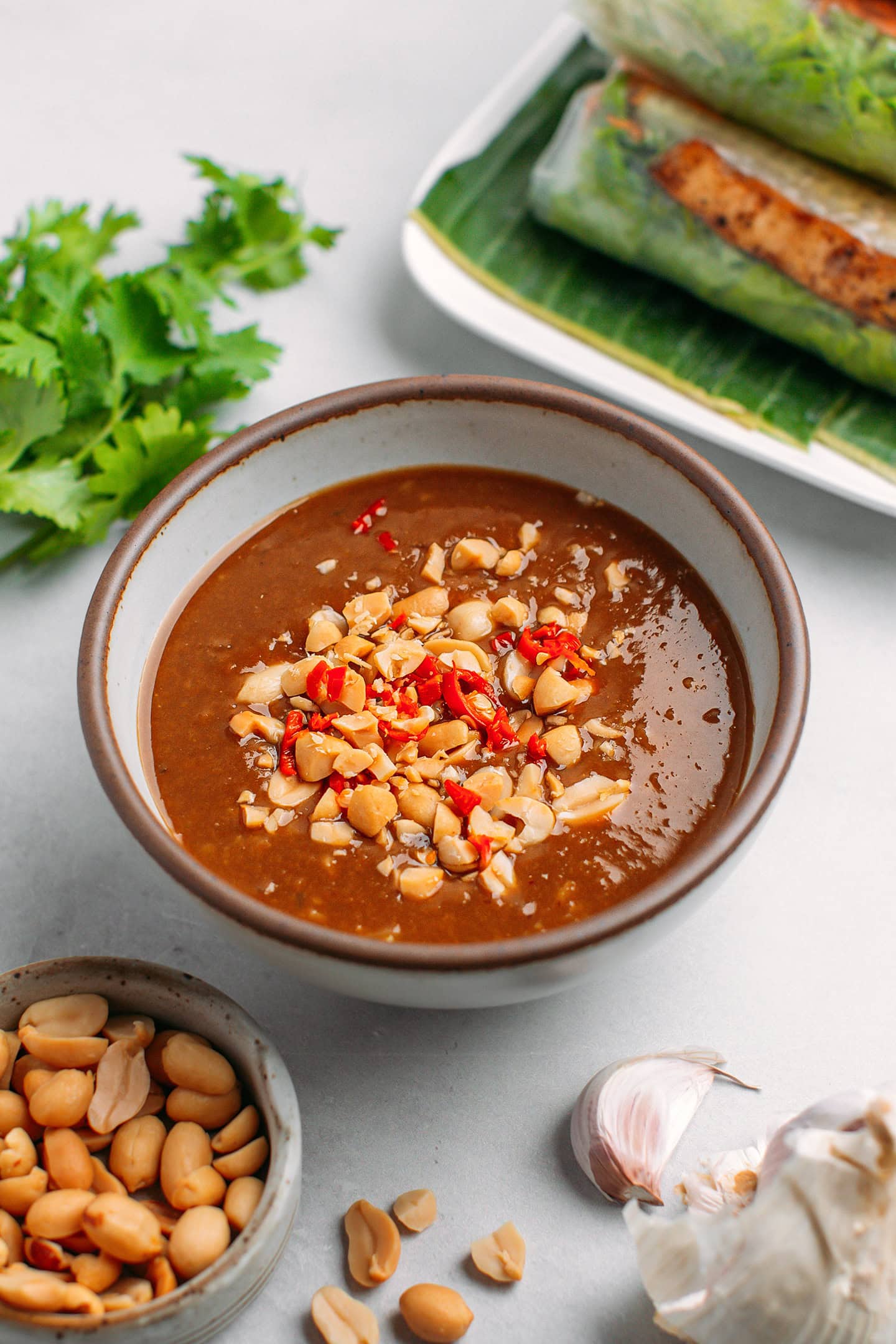 Peanut dipping sauce in a bowl, topped with crushed peanuts and chopped chili.