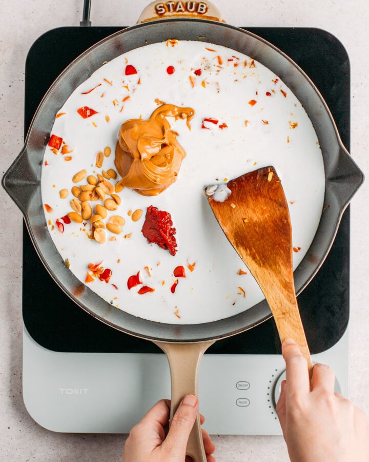 Stirring peanut butter and tomato paste into coconut milk in a skillet.