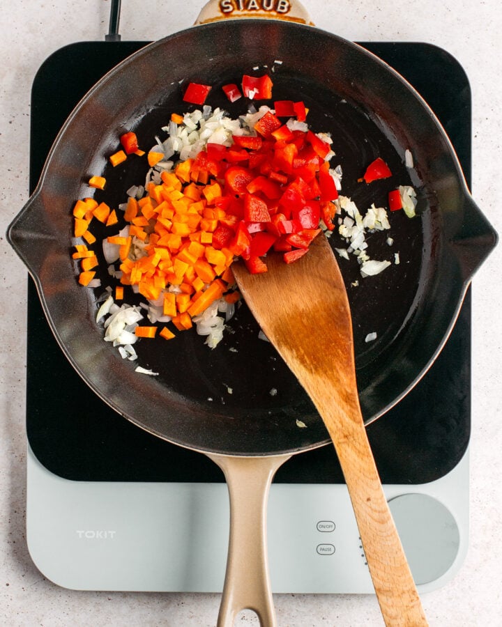 Diced carrots and red bell peppers in a skillet.