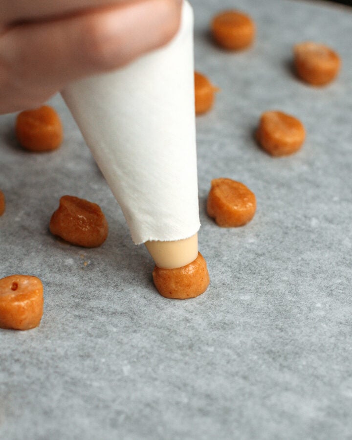 Piping a small ball of peanut butter batter on a baking sheet.