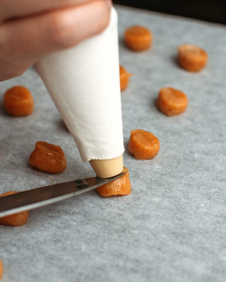 Using a knife to cut the batter coming out of a piping bag.