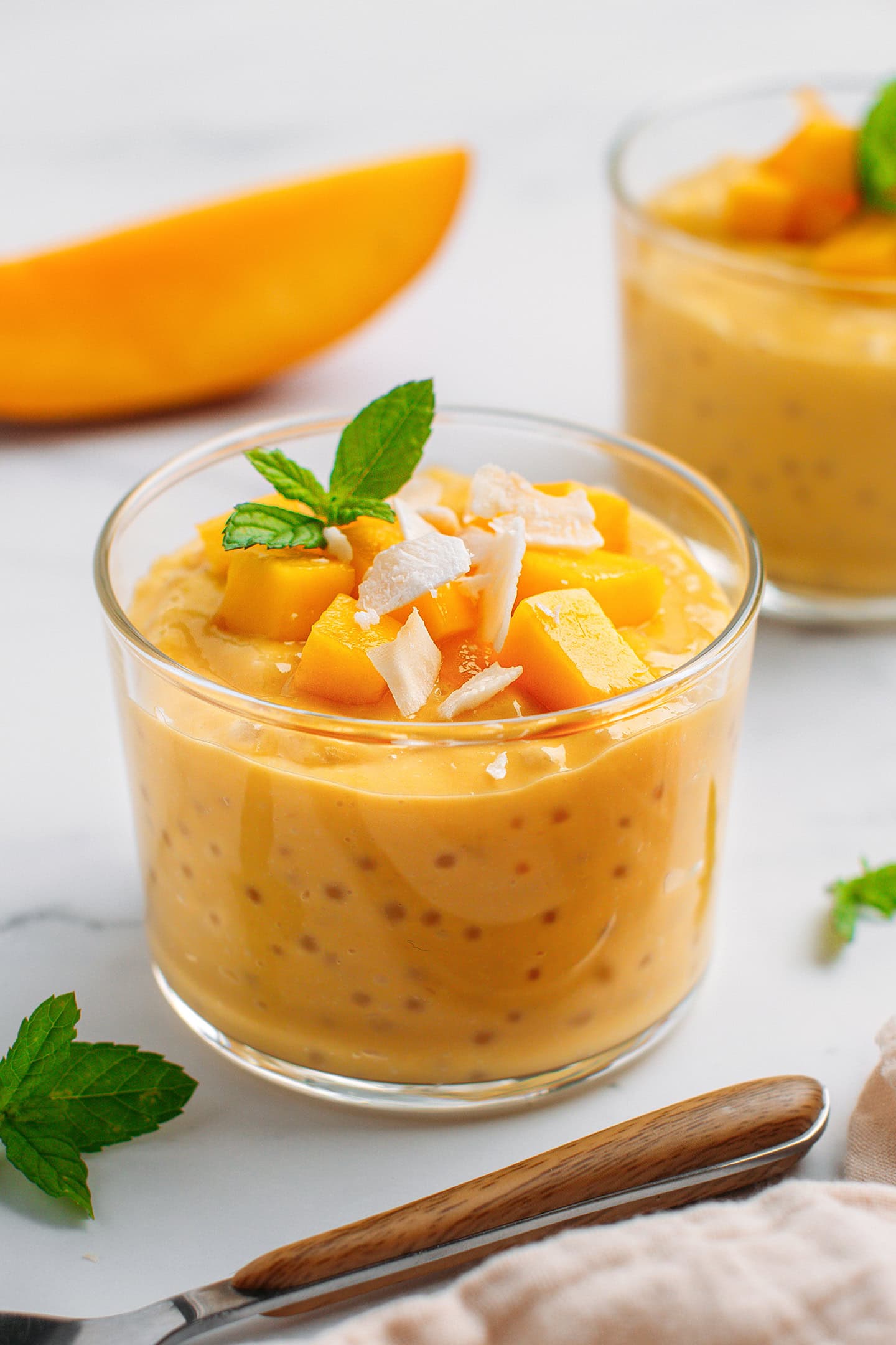 Mango sago in a ramekin garnished with chunks of mango, coconut flakes, and mint leaves.