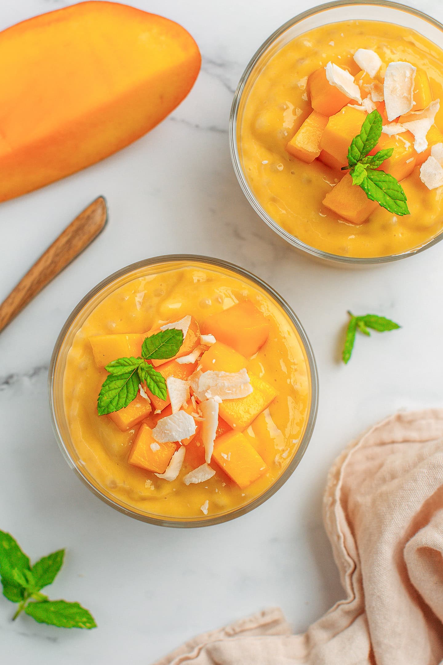 Top view of two ramekins filled with mango sago and topped with mango chunks, shredded coconut, and mint leaves.