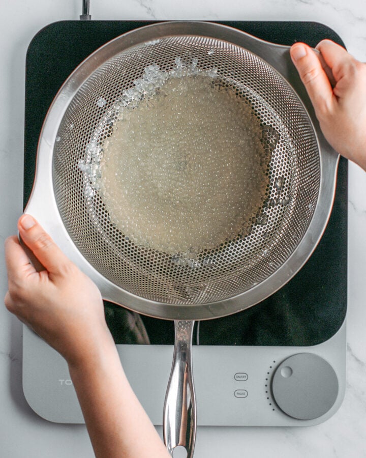 Draining cooked tapioca pearls using a colander.