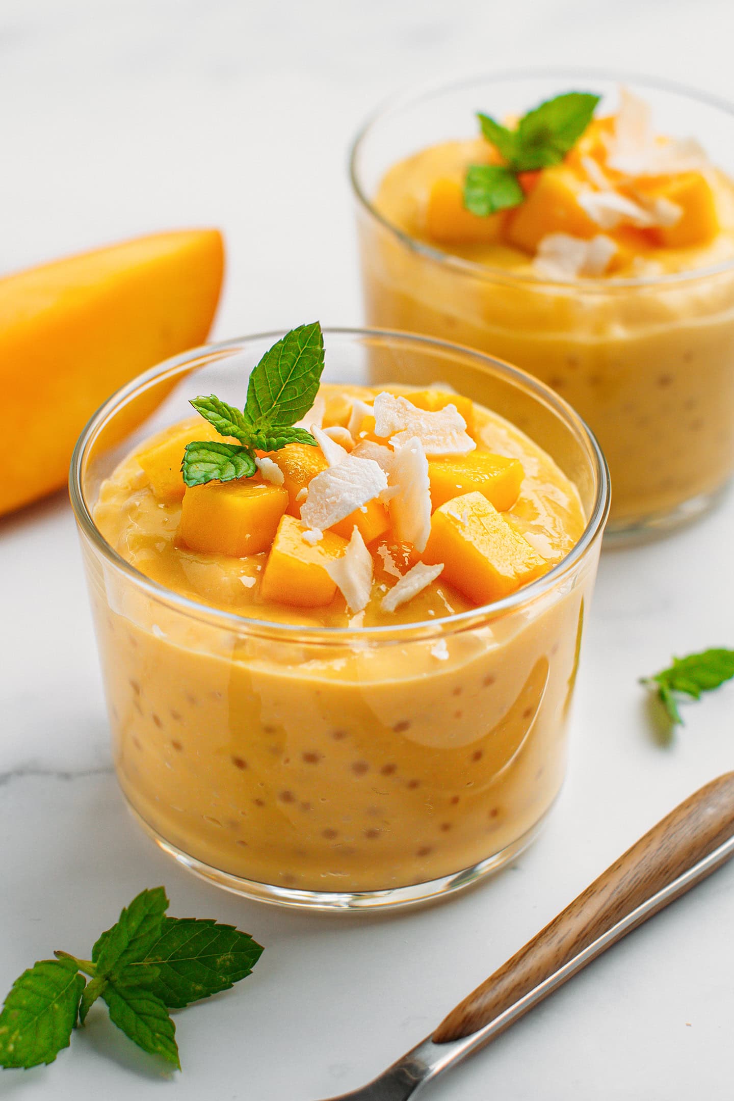 Mango sago topped with mango chunks, shredded coconut, and mint leaves in a ramekin.