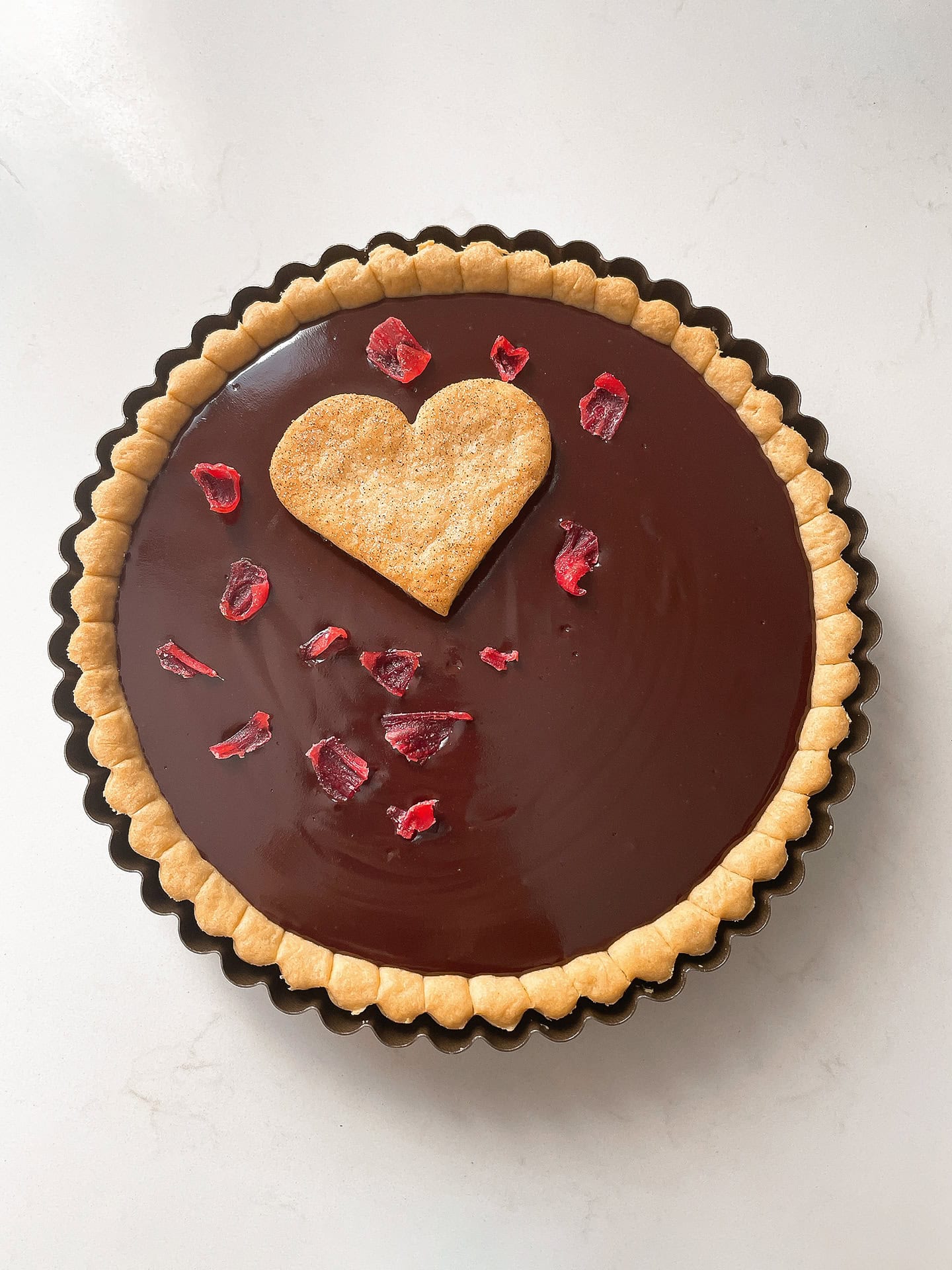 Creamy vegan chocolate tart topped with heart-shaped cookie and hibiscus.