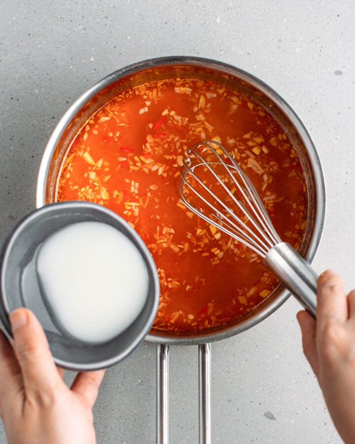 Pouring cornstarch slurry into a saucepan containing sweet and sour sauce.