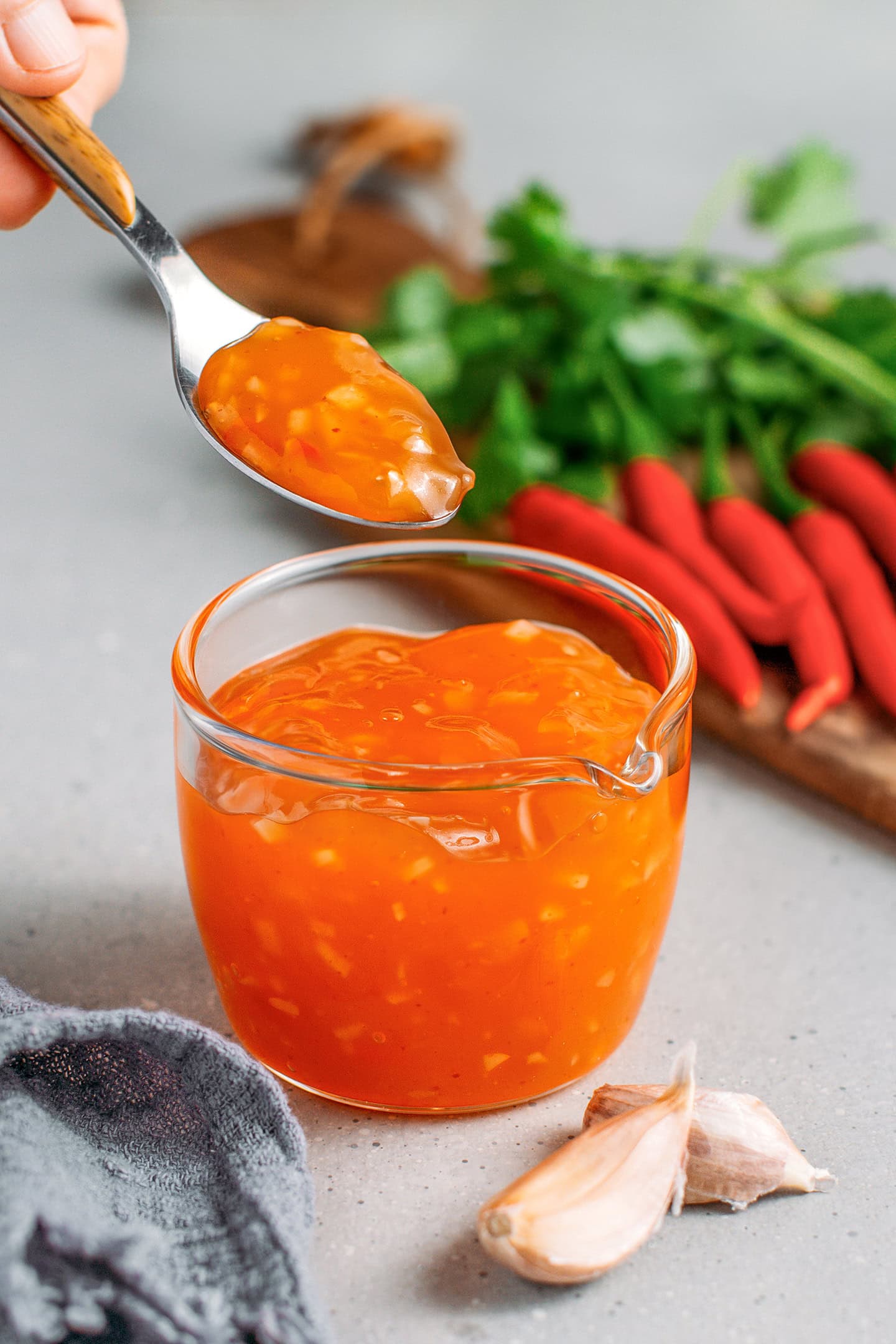 Holding a spoonful of sweet chili sauce over a small glass cup.