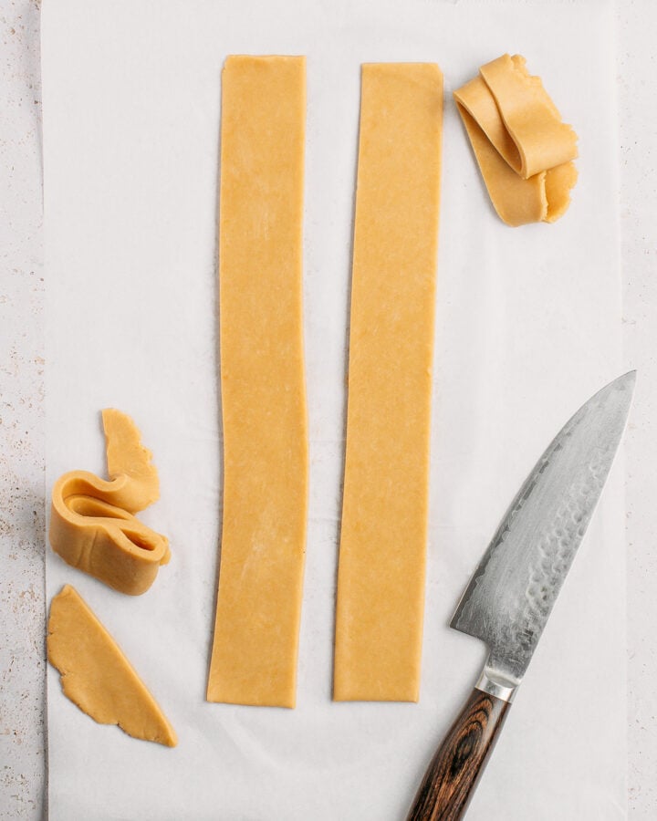 Two strips of pie crust dough on a layer of parchment paper.