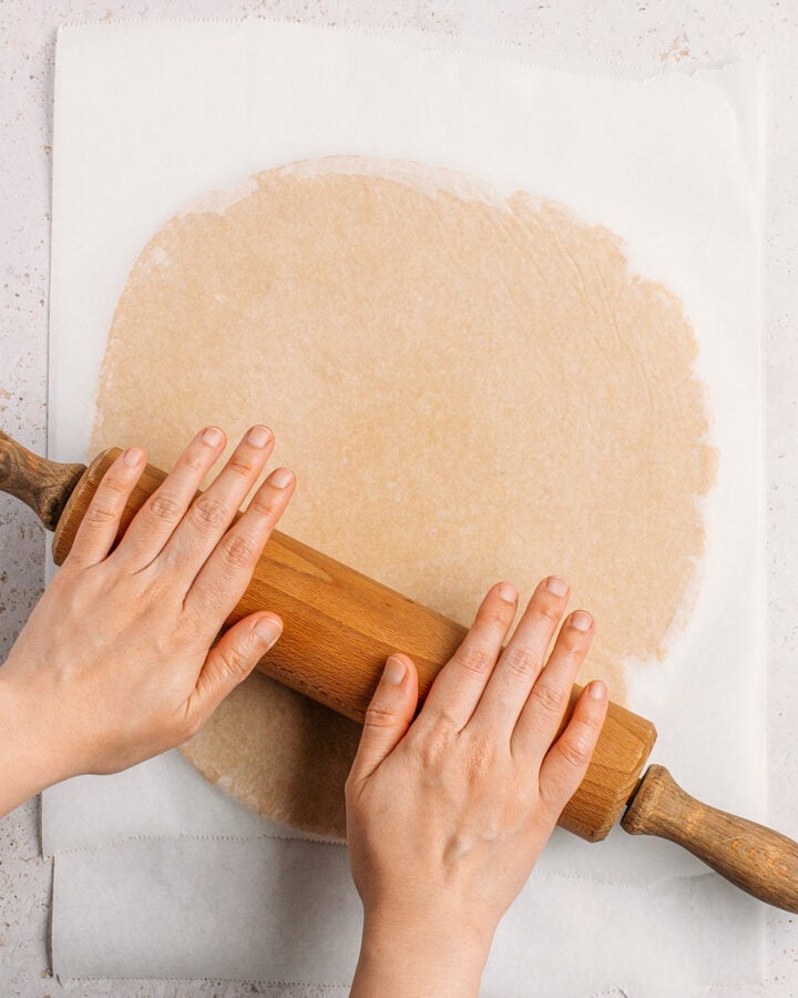 Flattening pie crust dough between two sheets of parchment paper.