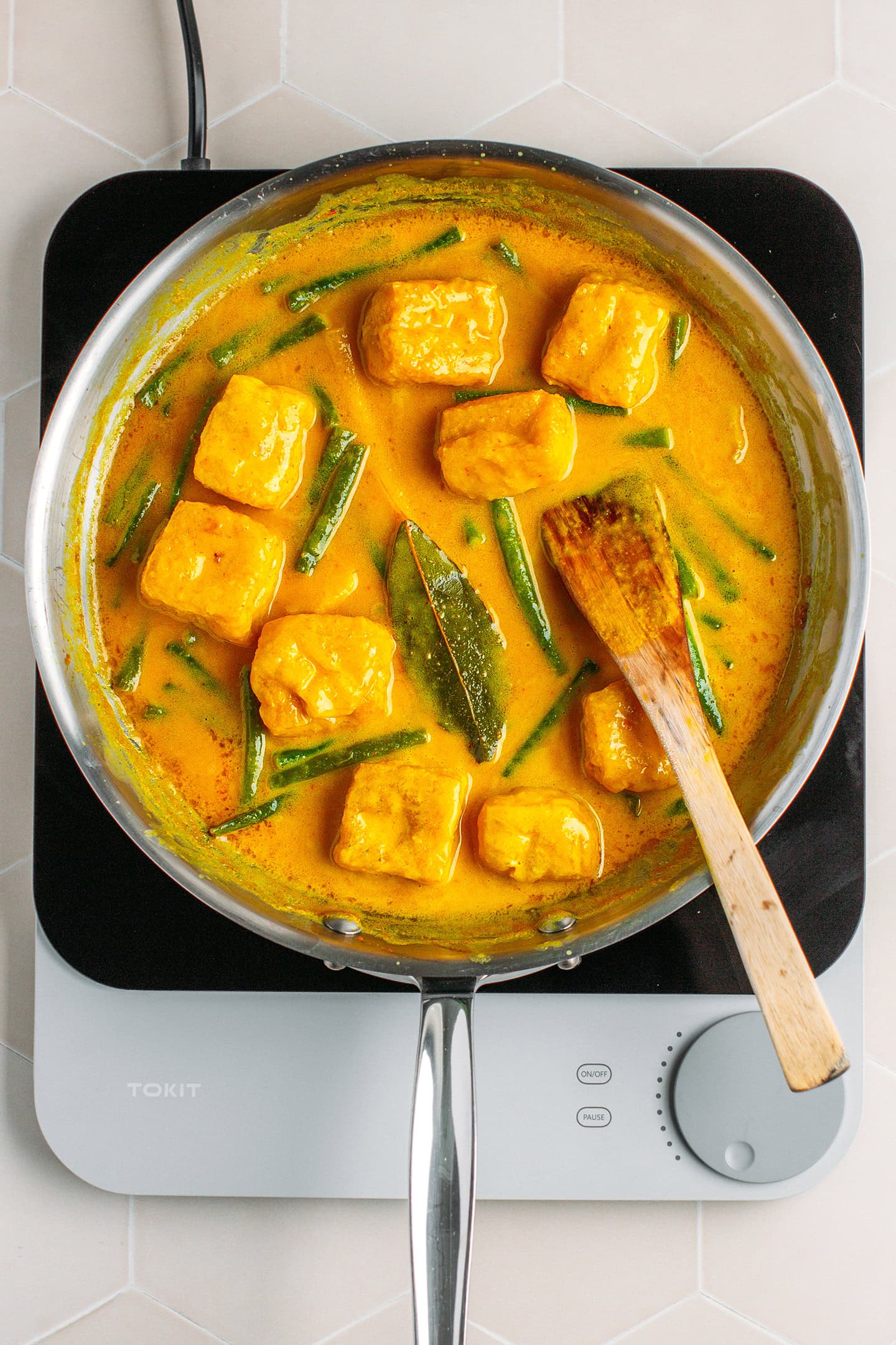 Cooked curry with green beans and tofu puffs in a skillet.