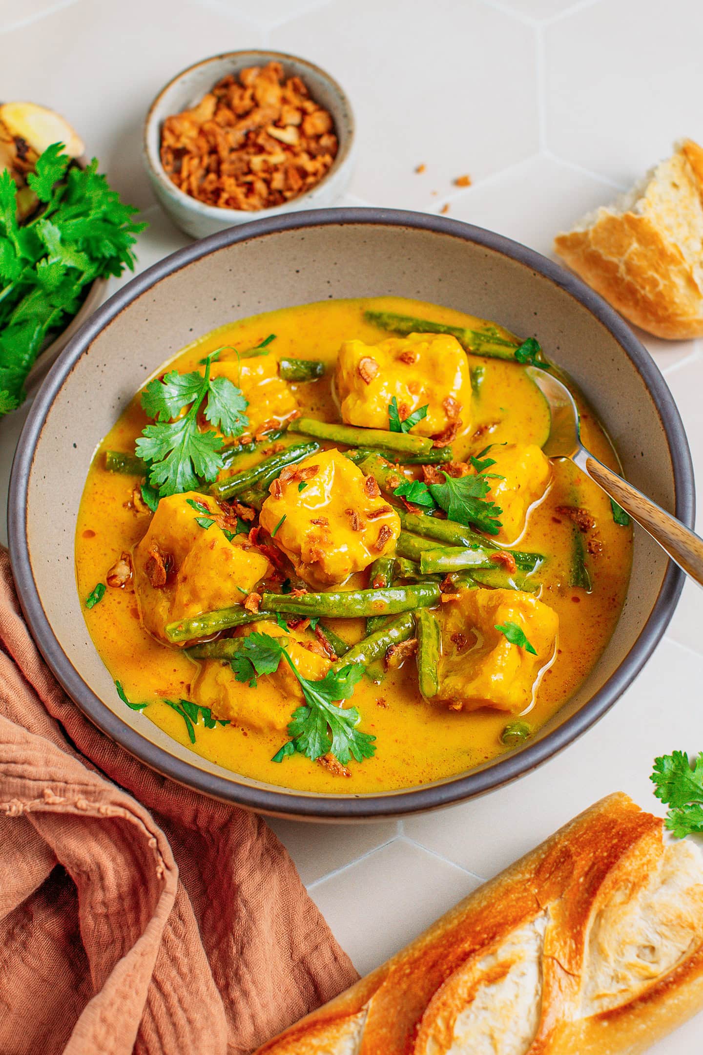 Curry with tofu, green beans, cilantro, and fried shallots in a deep bowl.