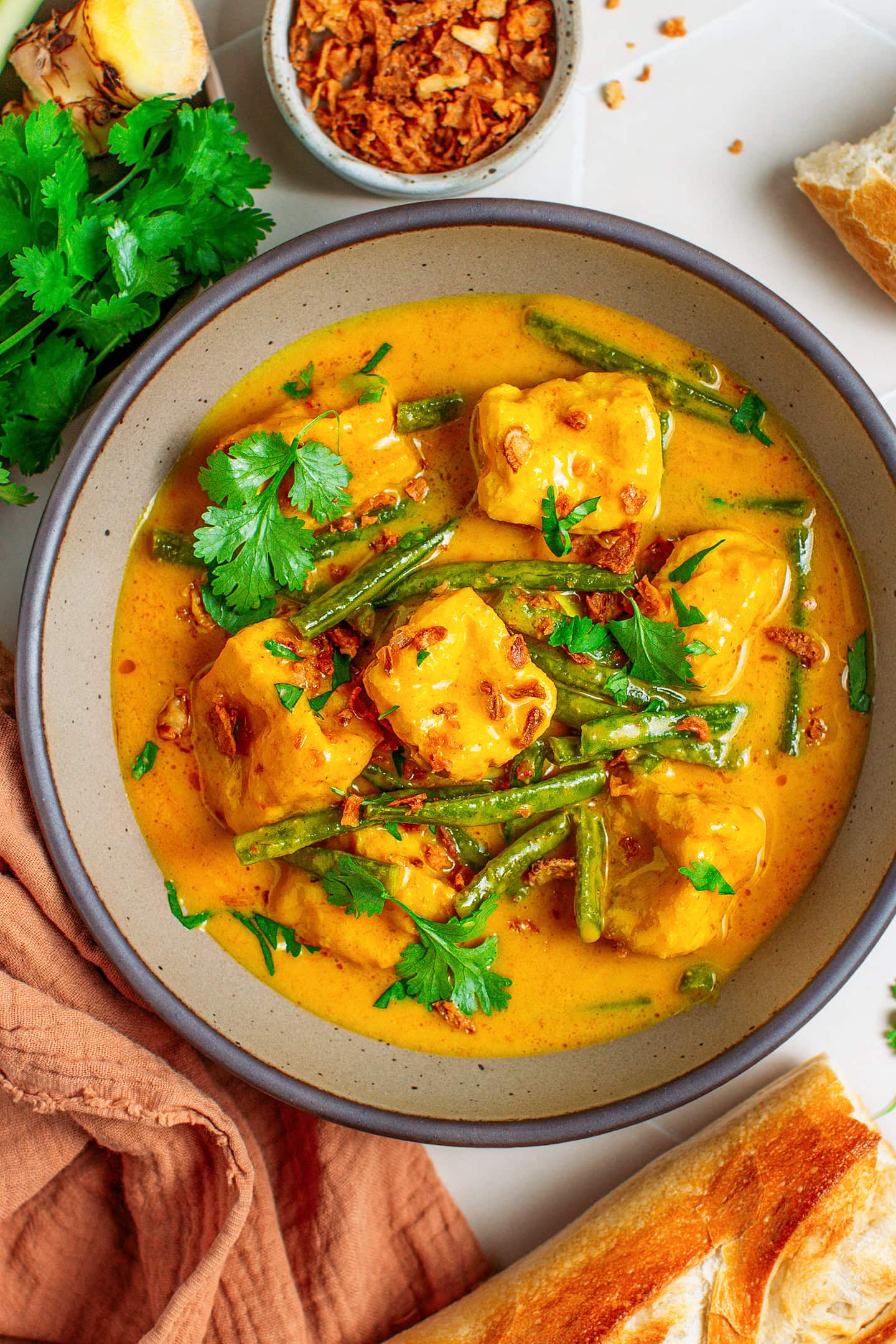 Indonesian curry with puffed tofu, green beans, cilantro, and fried shallots in a bowl.