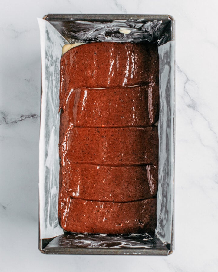 Chocolate cake batter piped over vanilla cake batter in a loaf pan.