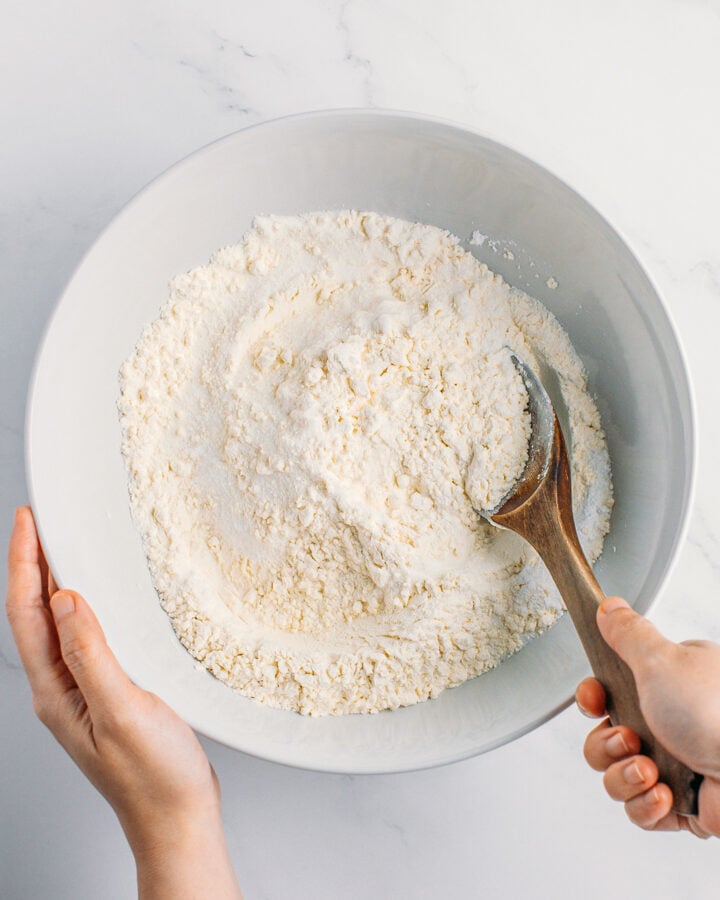 Stirring flour with sugar and baking powder in a mixing bowl.