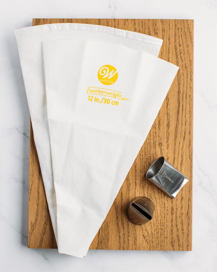 Two piping bags and two tips on a wooden board.