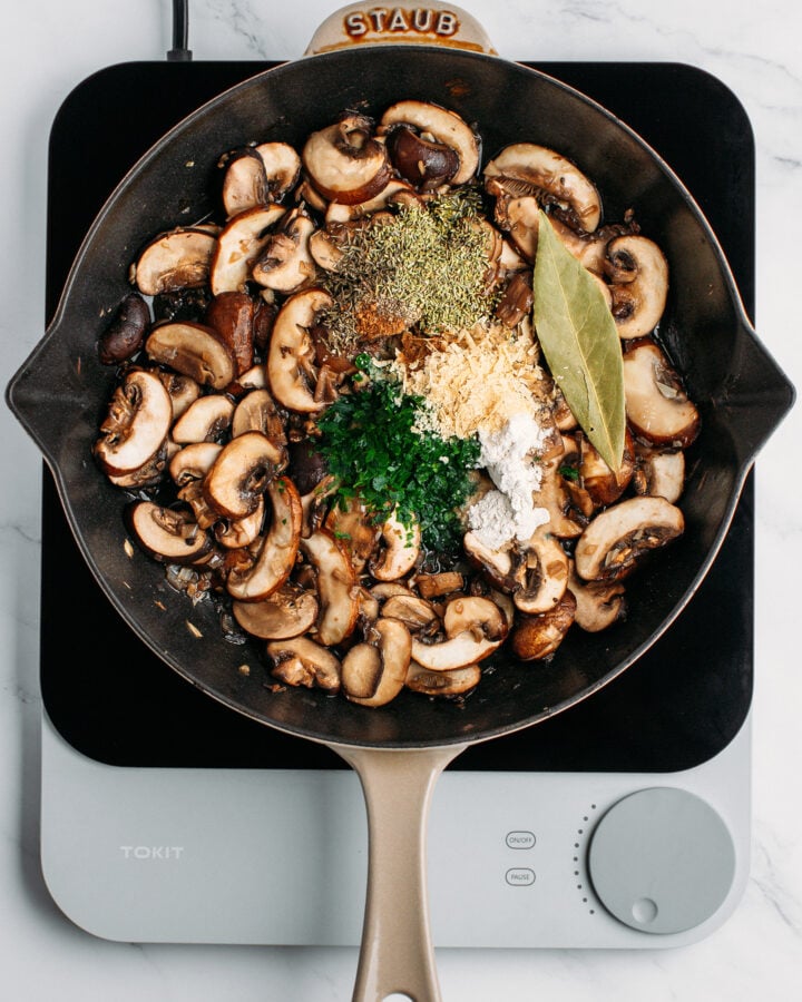 Sautéed mushrooms, fresh chopped parsley, bay leaf, and dried herbs in a skillet.