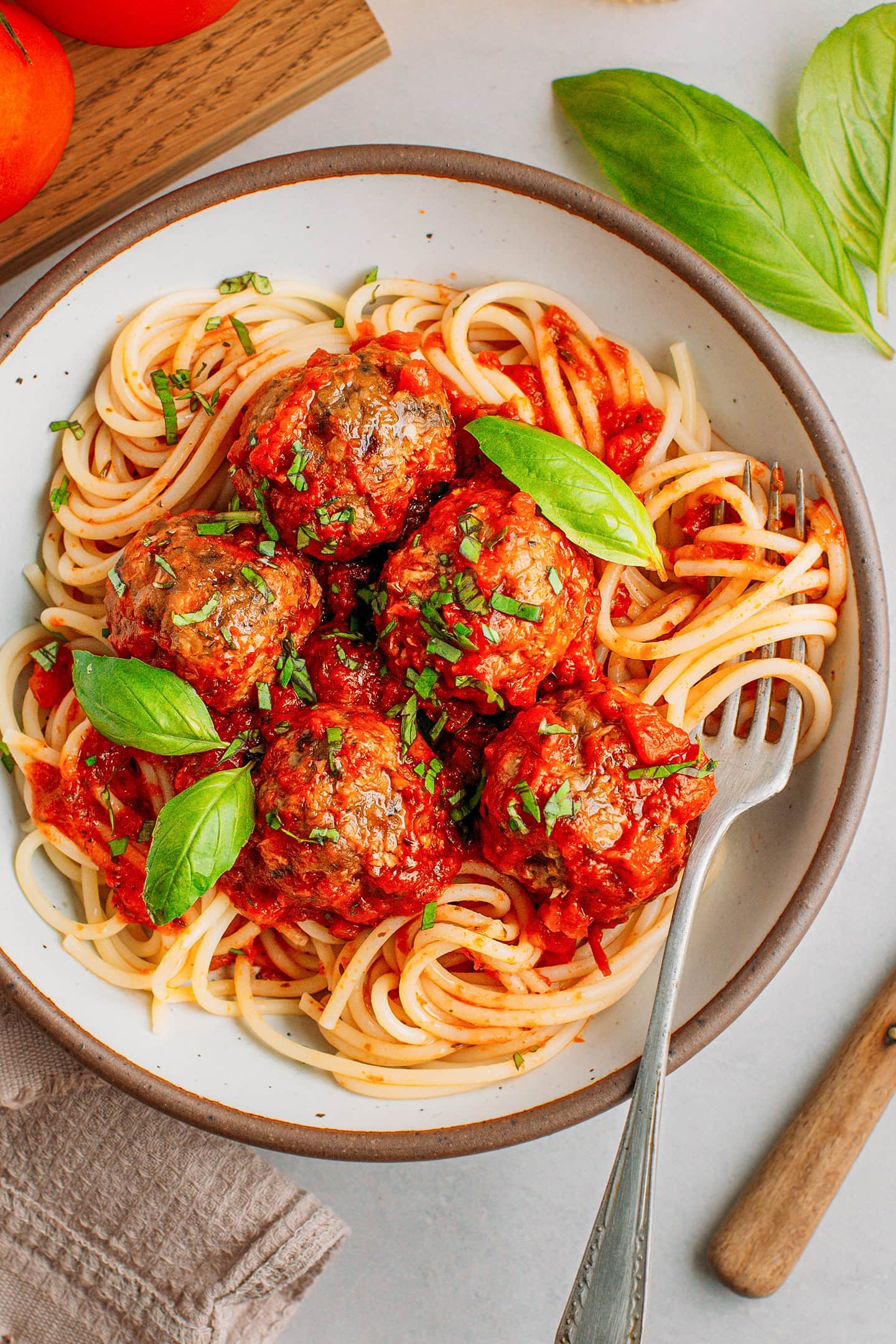 Five vegan meatballs with tomato sauce over spaghetti in a bowl.