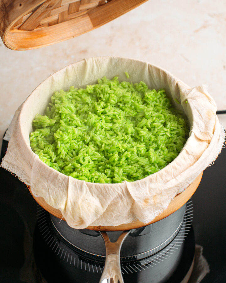 Cooked pandan sticky rice in a bamboo steamer basket.