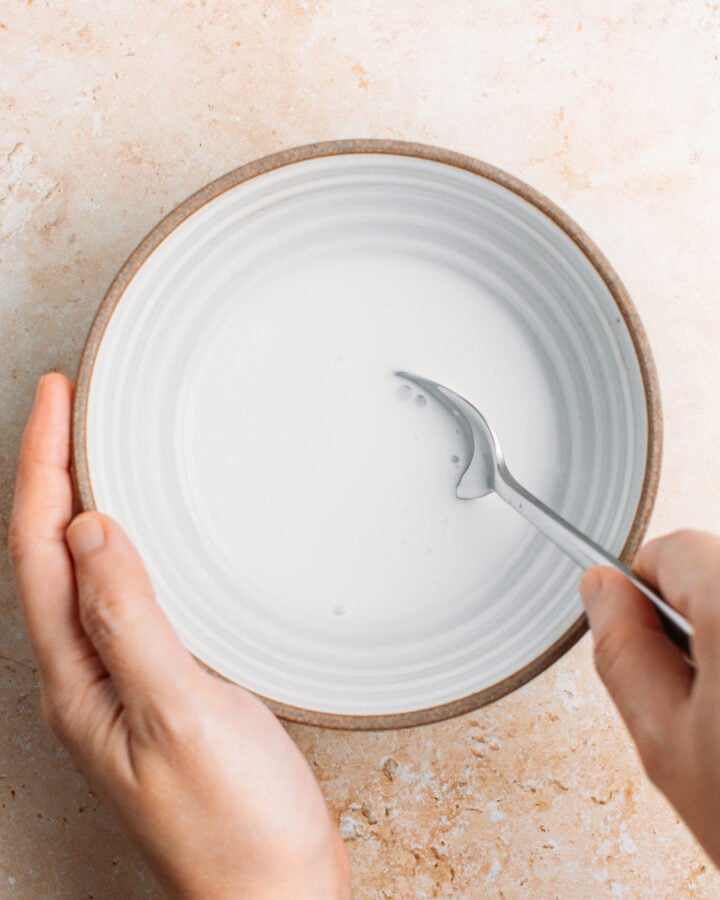 Stirring coconut milk with sugar and salt in a small bowl.