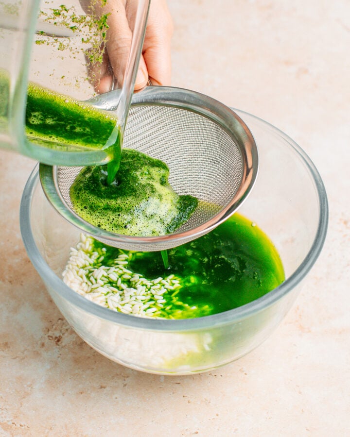 Straining pandan juice using a fine-sieve mesh.
