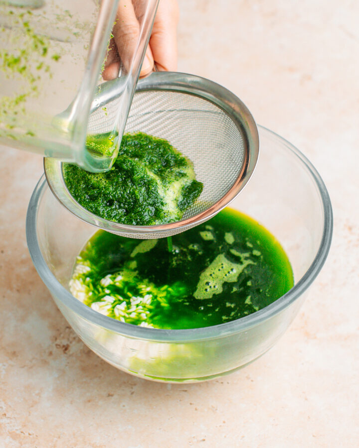 Straining pandan juice using a fine-sieve mesh.