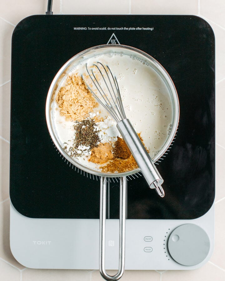 Coconut milk, nutritional yeast, dried thyme, and cumin in a saucepan.