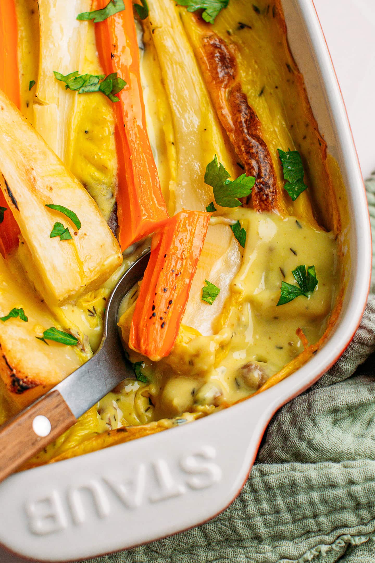 Spoonful of baked parsnips and carrots in a baking dish.