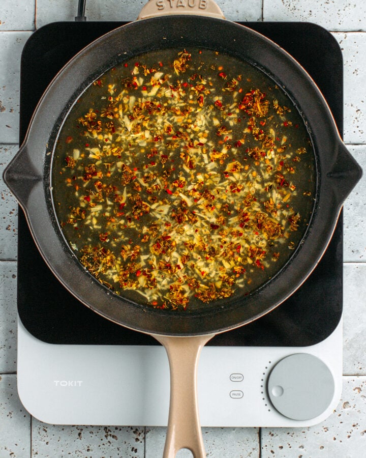 Sautéed garlic and vegetable broth in a skillet.