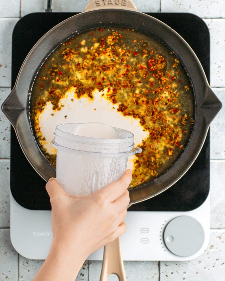Pouring cashew cream in a skillet containing vegetable broth.