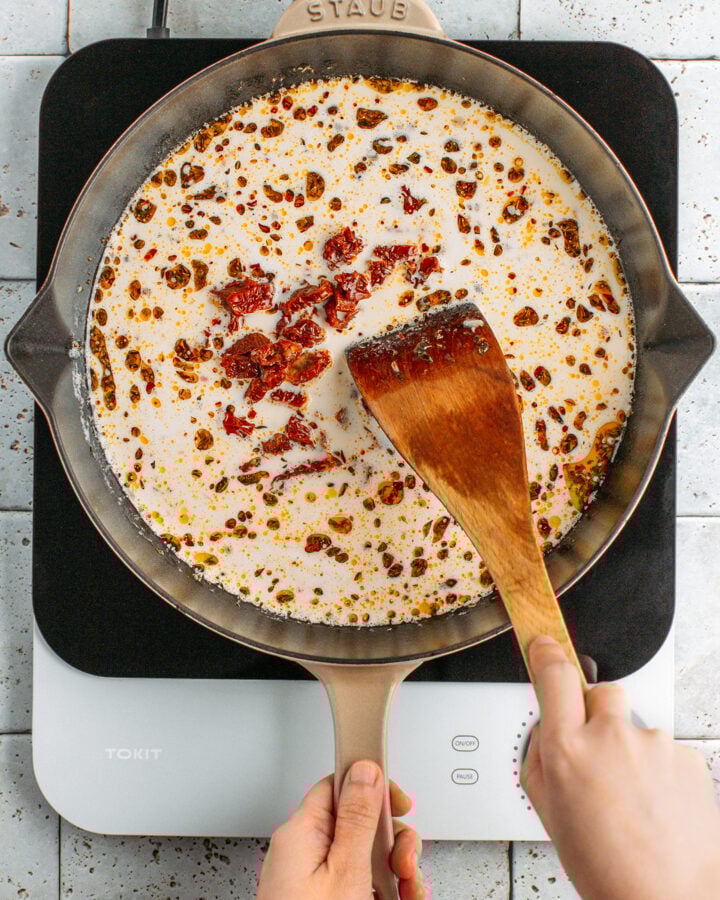 Stirring chopped dried tomatoes into a creamy sauce.