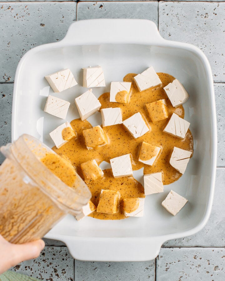 Pouring sun-dried tomato marinade other tofu cubes.