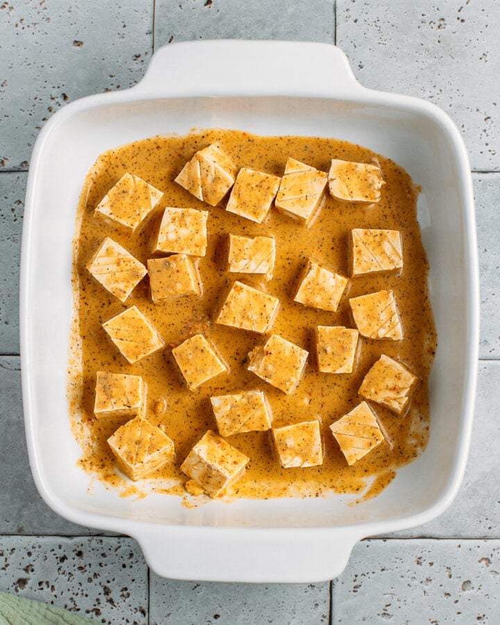 Tofu cubes coated with a sun-dried tomato marinade in a baking dish.
