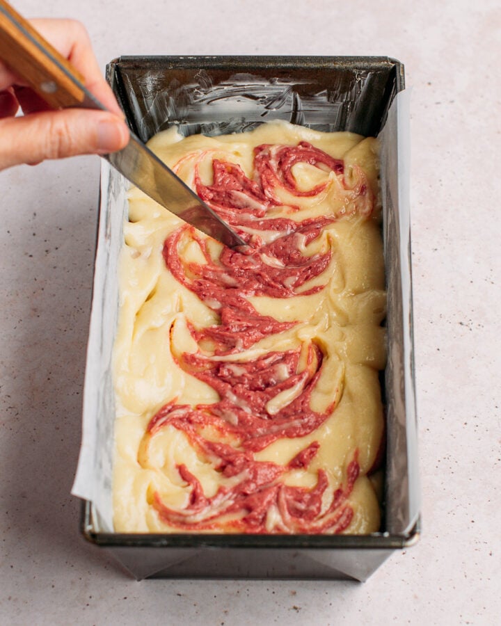 Swirling strawberry cake bater into vanilla cake batter in a loaf pan.