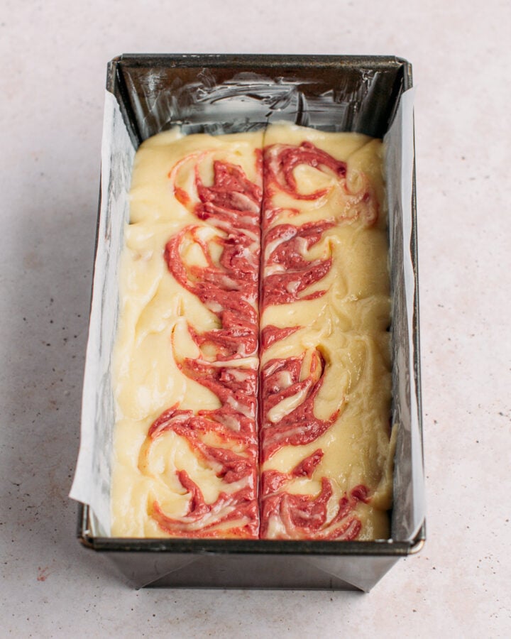 Strawberry cake batter swirled into vanilla cake batter in a loaf pan.