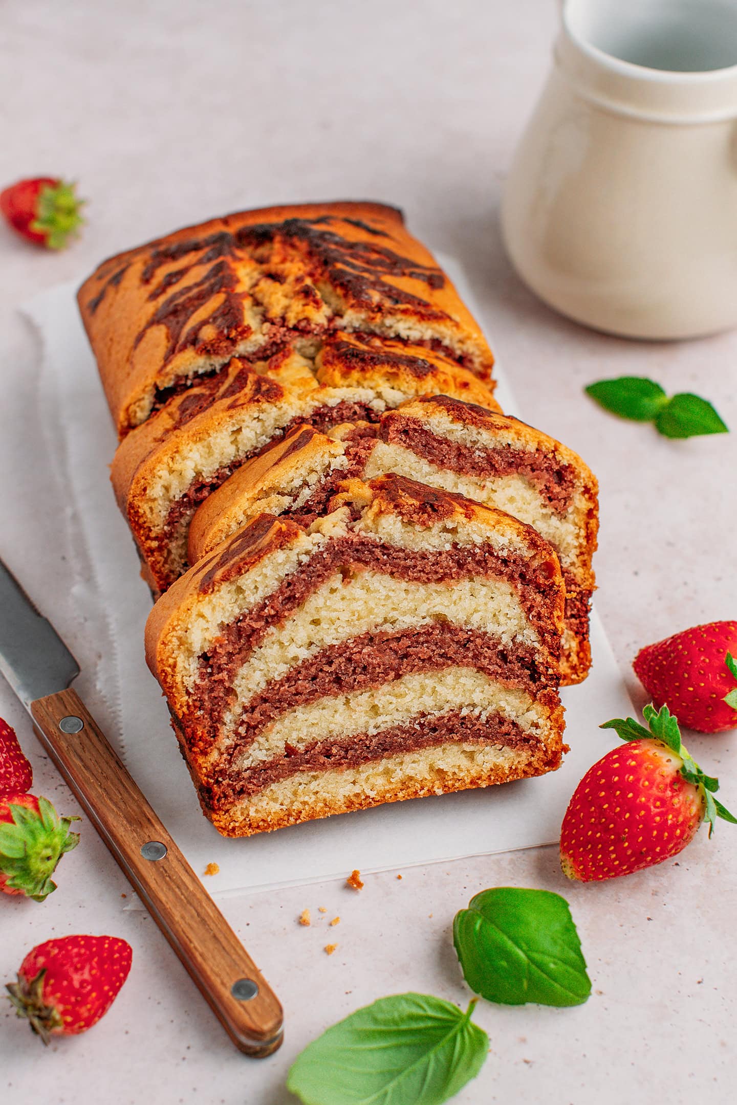 Sliced vanilla and strawberry marble cake with fresh strawberries around.