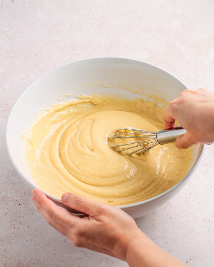 Creamy cake batter being whisked in a white bowl for baking.