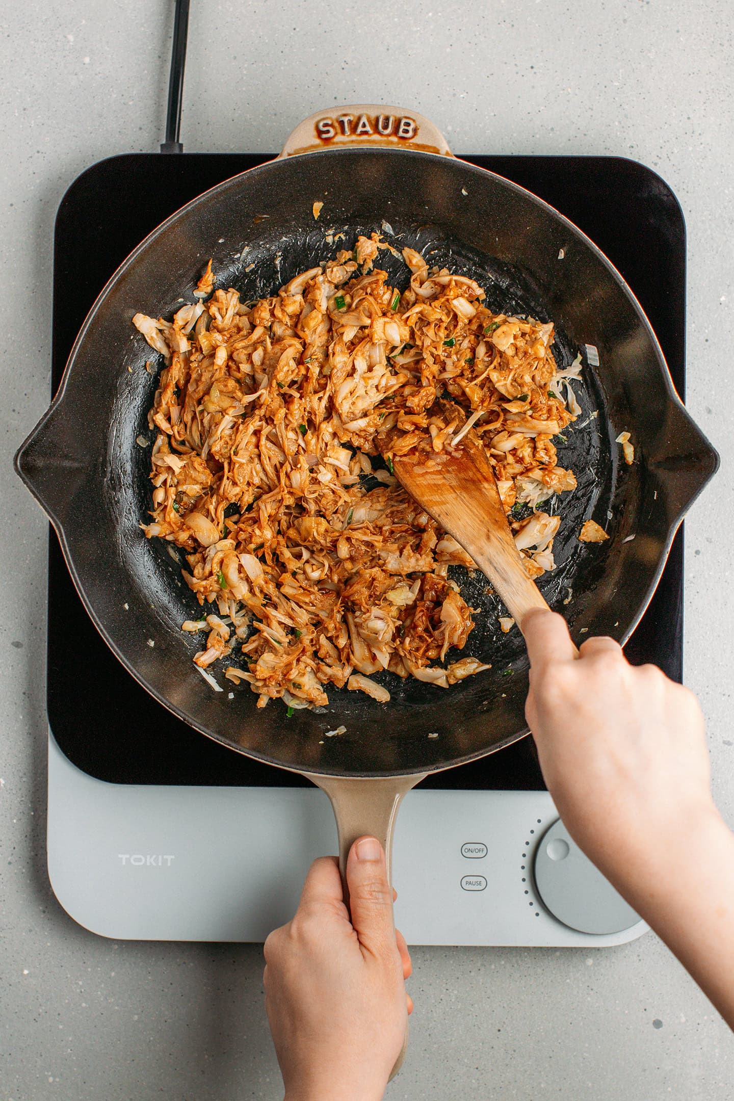 Tossing shredded jackfruit with soy sauce and five spice powder in a skillet.