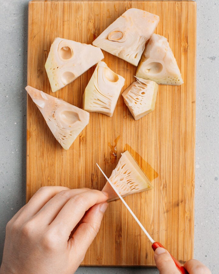 Slicing a piece of young green jackfruit on a cutting board.