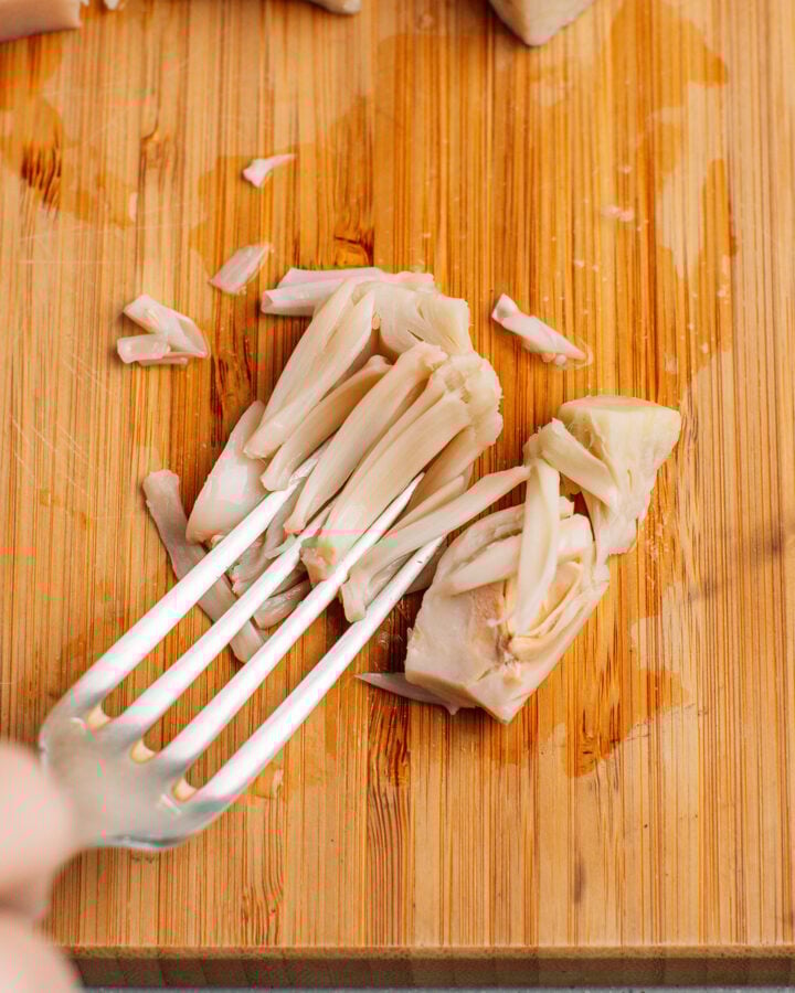 Shredding a piece of young green jackfruit using a fork.