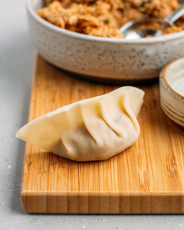 Wrapped, uncooked dumpling on a cutting board.