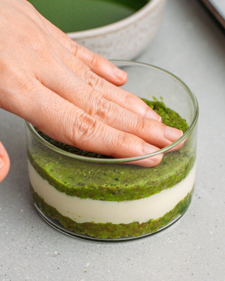 Pressing a layer of matcha sponge cake over a layer of vanilla cream in a ramekin.