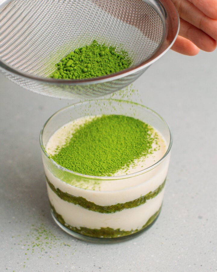 Dusting matcha powder over a ramekin filled with cream and sponge cake.